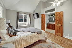 Bedroom with light wood-style flooring, vaulted ceiling, ceiling fan, and ensuite bath