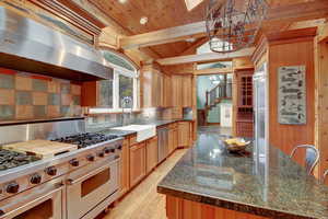 Kitchen featuring high end appliances, range hood, light wood finished floors, suspended lighting, and wooden ceiling