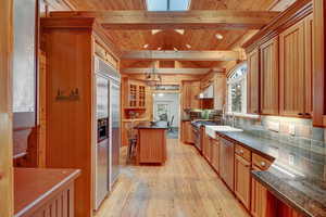 Kitchen featuring high end appliances, decorative backsplash, light wood-type flooring, glass insert cabinets, and decorative light fixtures