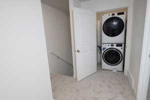 Laundry area featuring light colored carpet and stacked washer / dryer