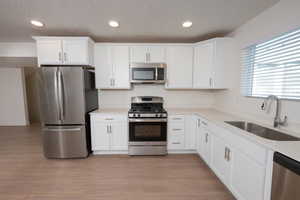 Kitchen with stainless steel appliances, white cabinets, light wood finished floors, recessed lighting, and a textured ceiling