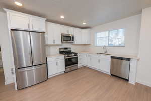 Kitchen with stainless steel appliances, white cabinets, recessed lighting, light wood finished floors, and a textured ceiling