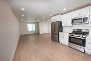 Kitchen featuring stainless steel appliances, white cabinetry, light wood-style floors, recessed lighting, and open floor plan