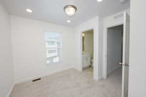 Unfurnished bedroom featuring light colored carpet, ensuite bathroom, and recessed lighting