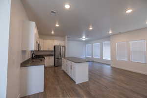 Kitchen with a center island, stainless steel appliances, white cabinets, open floor plan, and dark wood finished floors