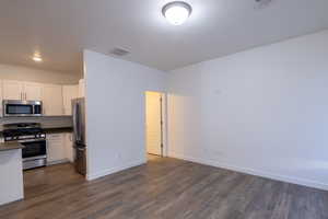 Kitchen featuring stainless steel appliances, dark countertops, white cabinets, and dark wood-style floors