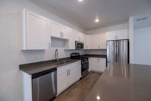 Kitchen featuring stainless steel appliances, white cabinets, dark wood-type flooring, and dark stone countertops