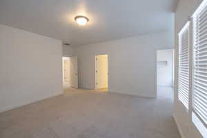 Unfurnished bedroom with a spacious closet, light colored carpet, and multiple windows
