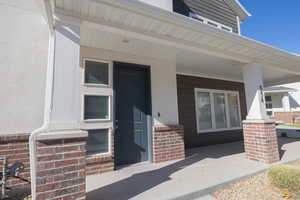 Doorway to property featuring covered porch, brick siding, and stucco siding