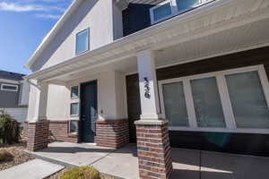 Doorway to property with covered porch, stucco siding, and brick siding