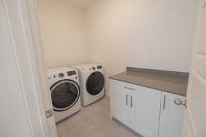 Laundry room featuring independent washer and dryer, light tile patterned floors, and cabinet space