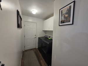 Laundry room featuring dark wood-type flooring, washing machine and clothes dryer, cabinet space, and a textured ceiling