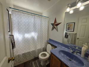 Full bath featuring vanity, shower / bath combo with shower curtain, and dark wood-type flooring