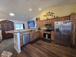 Kitchen with glass insert cabinets, stainless steel appliances, wood finish cabinets, a peninsula, and lofted ceiling