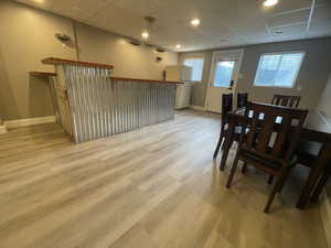 Dining area with a paneled ceiling, light wood-style flooring, a bar, and recessed lighting