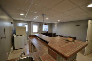 Kitchen featuring tile counters, freestanding refrigerator, a drop ceiling, washer / clothes dryer, and pendant lighting