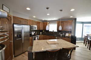Kitchen featuring stainless steel appliances, a kitchen island, a kitchen breakfast bar, hanging light fixtures, and light wood-type flooring