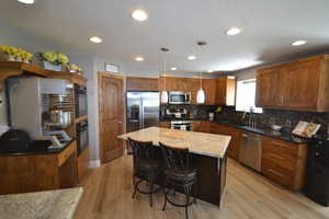 Kitchen featuring decorative light fixtures, a breakfast bar area, stainless steel appliances, a center island, and light wood-type flooring