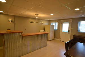 Kitchen with freestanding refrigerator, a paneled ceiling, a kitchen breakfast bar, light wood-type flooring, and recessed lighting