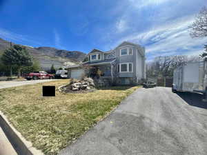 View of front of property with asphalt driveway, a mountain view, stone siding, and a front yard