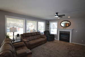 Living room featuring a ceiling fan, a glass covered fireplace, carpet, and a textured ceiling