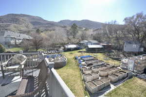 View of green lawn featuring a vegetable garden, a deck with mountain view, and an outbuilding off primary bedroom