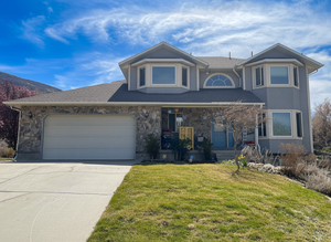 View of front of home featuring covered porch, a front lawn, stone siding, and concrete driveway AI enhanced