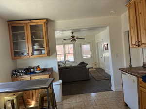 Kitchen featuring dishwasher, dark countertops, glass fronted cabinets, wood finish cabinetry, and a ceiling fan