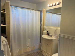 Bathroom featuring vanity, shower / bathtub combination with curtain, a textured ceiling, a wainscoted wall, and a textured wall