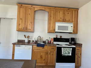 Kitchen featuring white appliances, dark countertops, and wood finish cabinetry