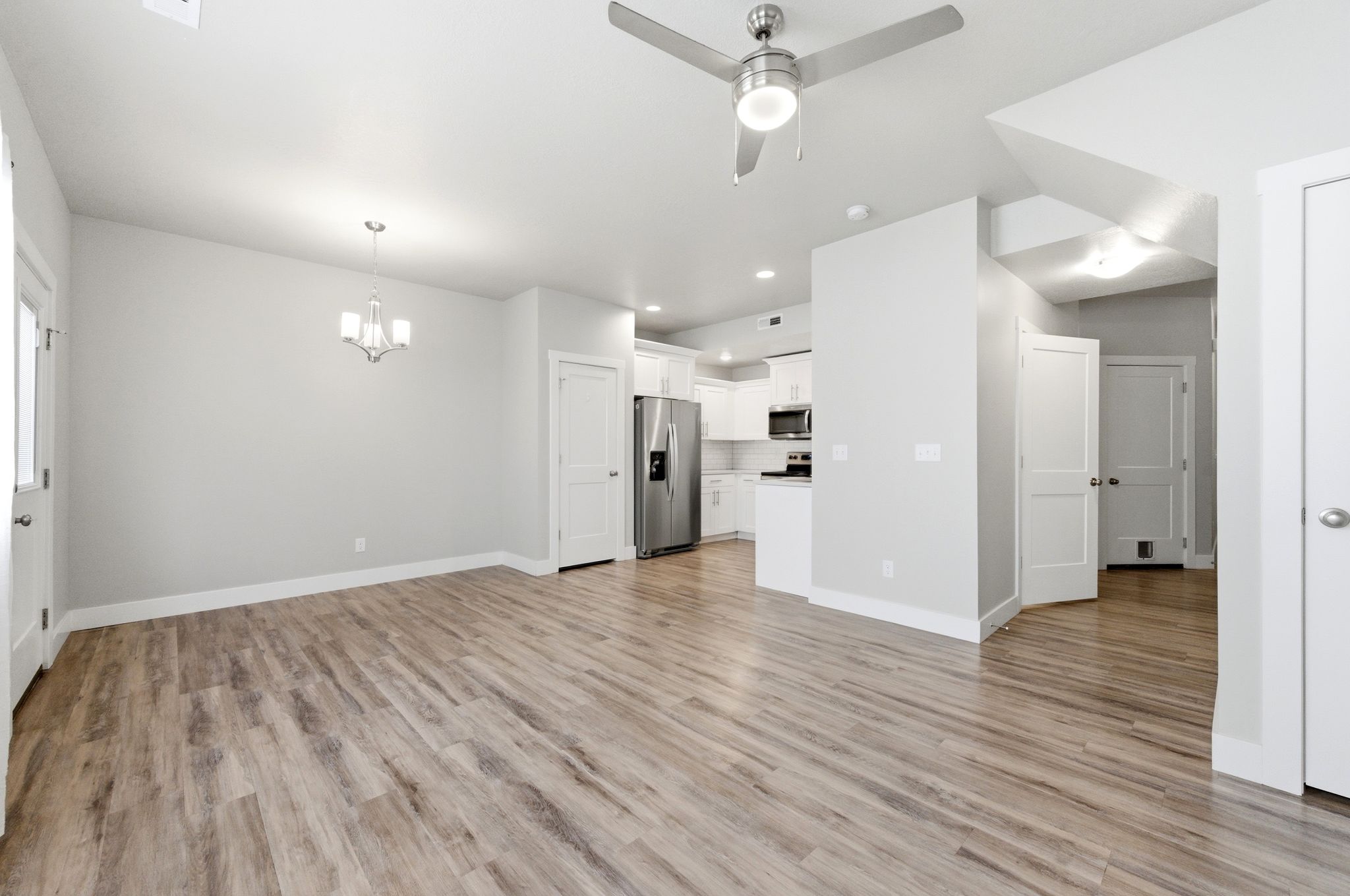 Unfurnished living room featuring a ceiling fan, hanging lights, and light wood-style floors