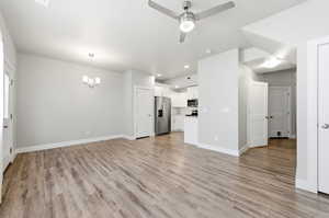 Unfurnished living room featuring a ceiling fan, hanging lights, and light wood-style floors