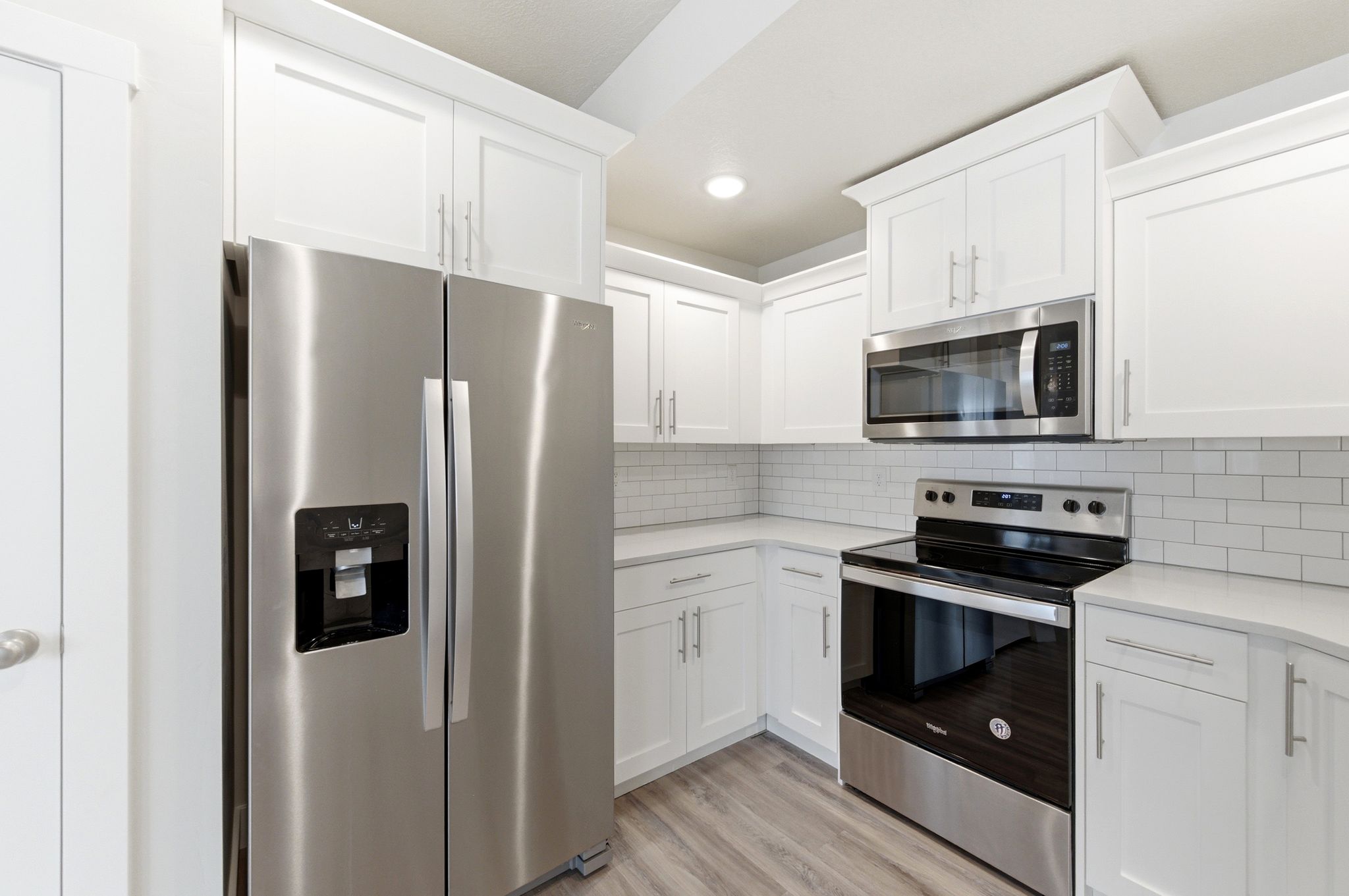 Kitchen featuring stainless steel appliances, white cabinets, light wood finished floors, recessed lighting, and backsplash