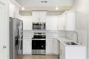 Kitchen featuring stainless steel appliances, white cabinets, light stone counters, light wood-style floors, and recessed lighting
