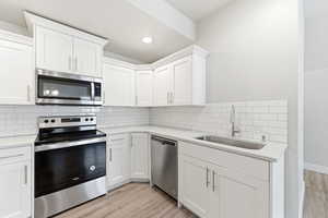 Kitchen featuring stainless steel appliances, light wood-type flooring, white cabinetry, and light stone countertops