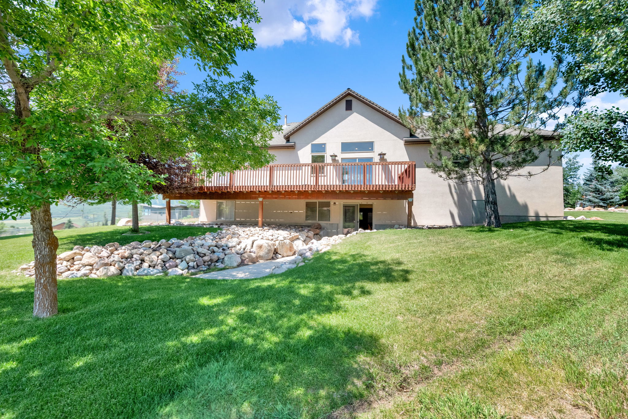 Back of property with a deck, a lawn, and stucco siding