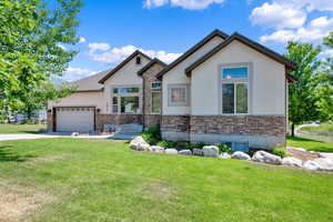 View of front of home featuring stone siding, a front lawn, and stucco siding