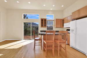 Kitchen featuring glass fronted cabinets, white appliances, recessed lighting, a kitchen breakfast bar, and light wood-style flooring