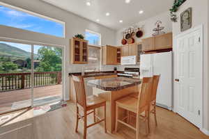 Kitchen featuring white appliances, glass fronted cabinets, light wood-style flooring, a kitchen breakfast bar, and recessed lighting
