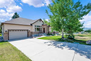 View of front of house with stucco siding, a front yard, stone siding, a garage, and driveway