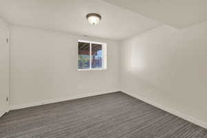 Spare room featuring dark colored carpet and baseboards
