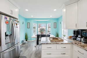 Kitchen with stainless steel fridge with ice dispenser, white cabinets, light countertops, light wood finished floors, and recessed lighting