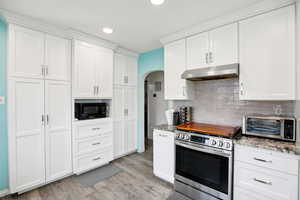 Kitchen with arched walkways, stainless steel range oven, white cabinetry, black microwave, and light stone counters