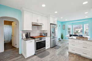 Kitchen featuring light countertops, stainless steel appliances, white cabinetry, arched walkways, and recessed lighting