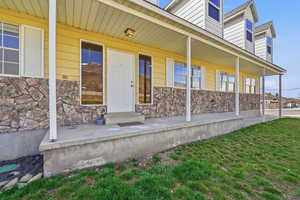 Doorway to property featuring covered porch, stone siding, and a lawn