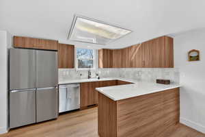 Kitchen with a peninsula, stainless steel appliances, light stone counters, wood finish cabinetry, and modern cabinets