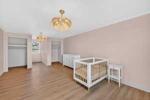 Bedroom with multiple closets, light wood-style flooring, and crown molding