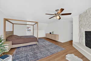 Bedroom featuring a fireplace, ornamental molding, wood finished floors, and ceiling fan