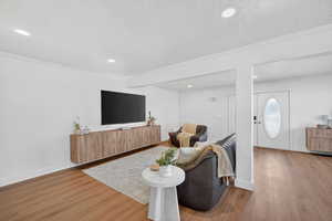 Living area featuring light wood-type flooring, crown molding, a textured ceiling, and recessed lighting