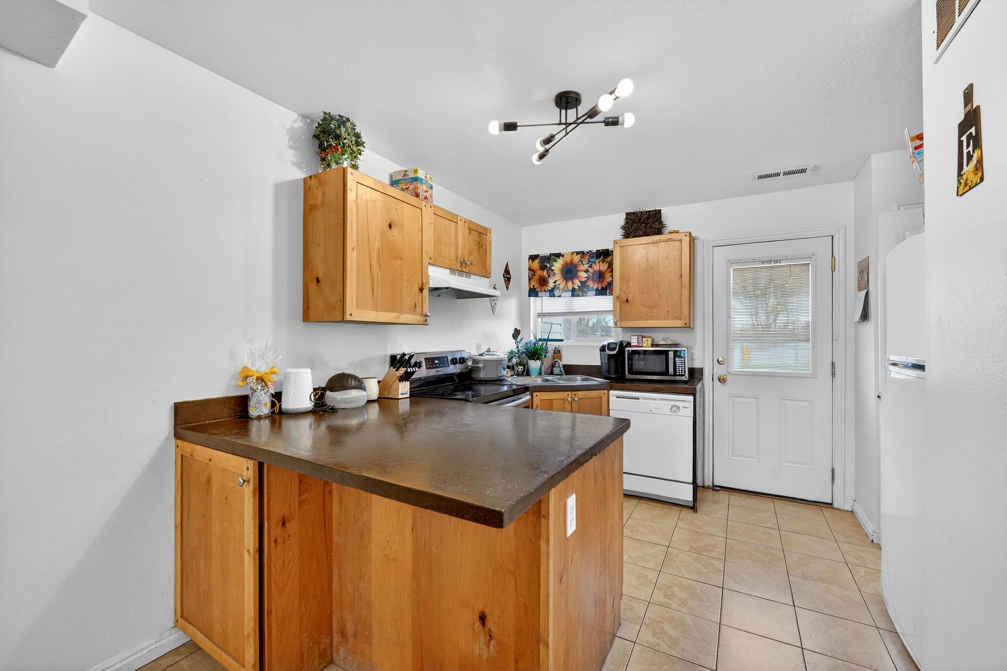 Kitchen with a peninsula, stainless steel appliances, dark countertops, light tile patterned floors, and light wood finish cabinets